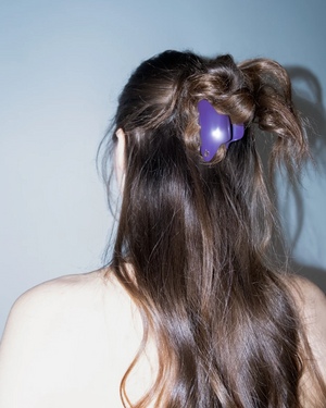 Person with long hair styled in pigtails with a purple hair clip against a light blue background
