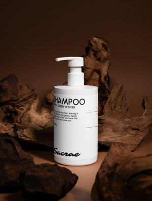 Sacrae Gloss Shampoo Smoky Green Vetiver — editorial shot with driftwood on warm brown backdrop