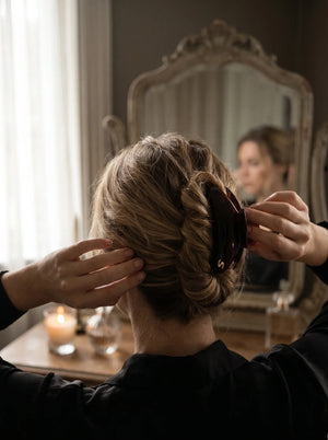 Model wearing Sacrae Lumière Medium Hair Clip in Tortoise, twisted updo at a vanity mirror